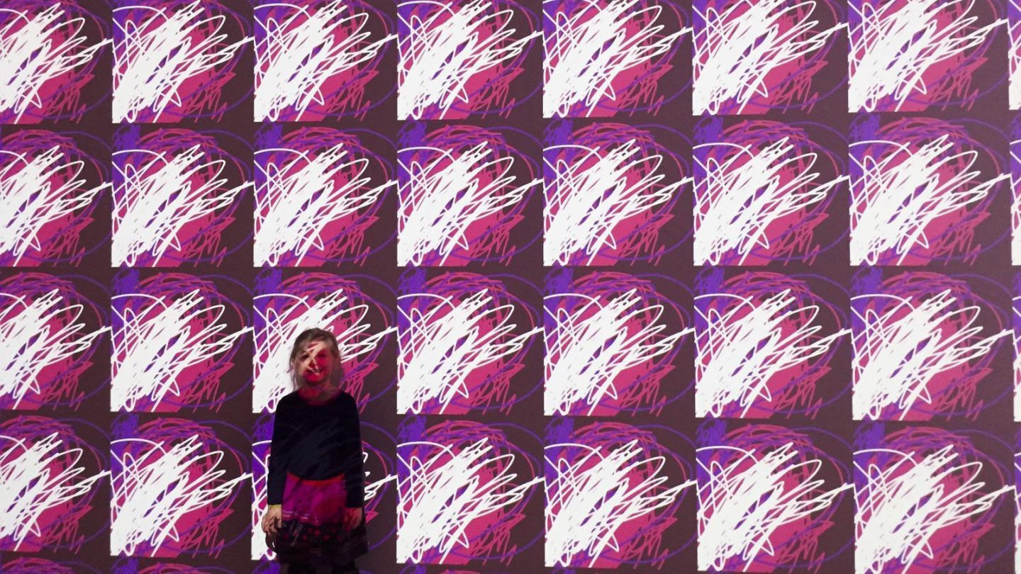 A child stands in front of a wall filled with a repeated pattern she created